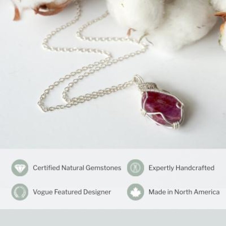 May include: A silver chain necklace featuring a wire-wrapped, irregular, deep pink gemstone pendant. Below the jewelry, text reads: Certified Natural Gemstones, Expertly Handcrafted, Vogue Featured Designer, and Made in North America.