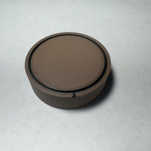 Może przedstawiać: Okrągły brązowy gałka z czarnym pierścieniem wokół krawędzi.