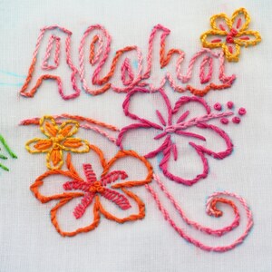 May include: Embroidered white fabric with the word "Aloha" in pink and orange thread. The word is surrounded by pink and orange hibiscus flowers.