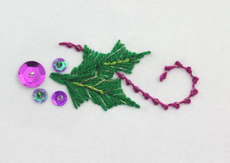 May include: Embroidered green holly leaf with gold thread accents and pink and purple sequins.