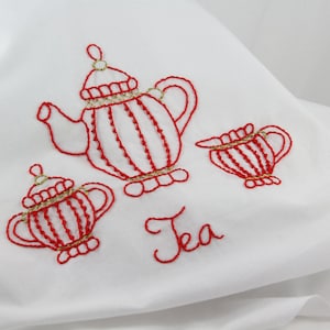 May include: Red embroidered tea set with a teapot, creamer, and sugar bowl. The embroidery is done in a simple, elegant style. The word "Tea" is embroidered below the set.