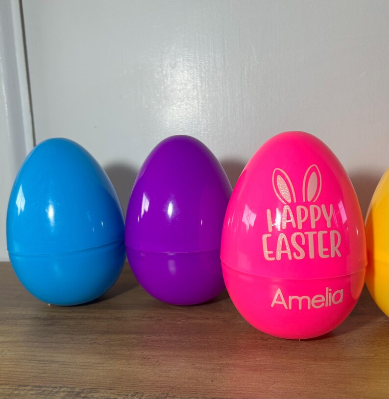 May include: Four plastic Easter eggs, one blue, one purple, one pink with "Happy Easter" and "Amelia" written on it, and one yellow.