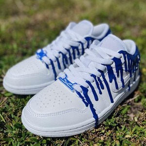 May include: White low-top trainers with blue paint dripping down the sides. The paint is a bright blue and creates a unique design.