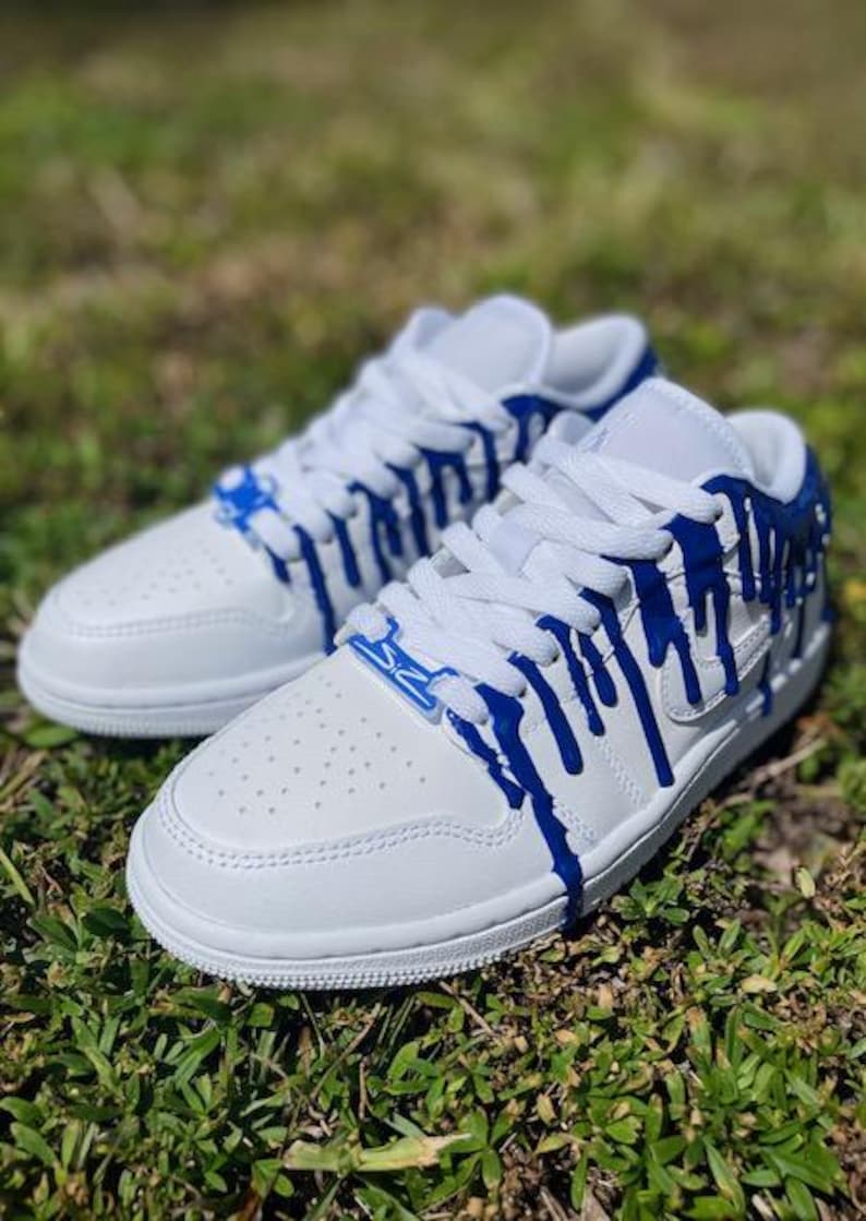 May include: White low-top trainers with blue paint dripping down the sides. The paint is a bright blue and creates a unique design.