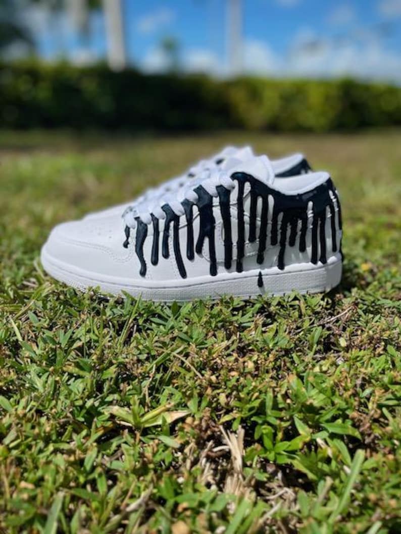 May include: White trainers with black paint dripping down the sides. The paint looks like it is melting down the shoe.