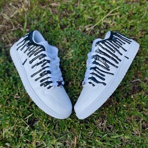 May include: White trainers with black paint dripping down the sides. The paint is in a vertical stripe pattern.