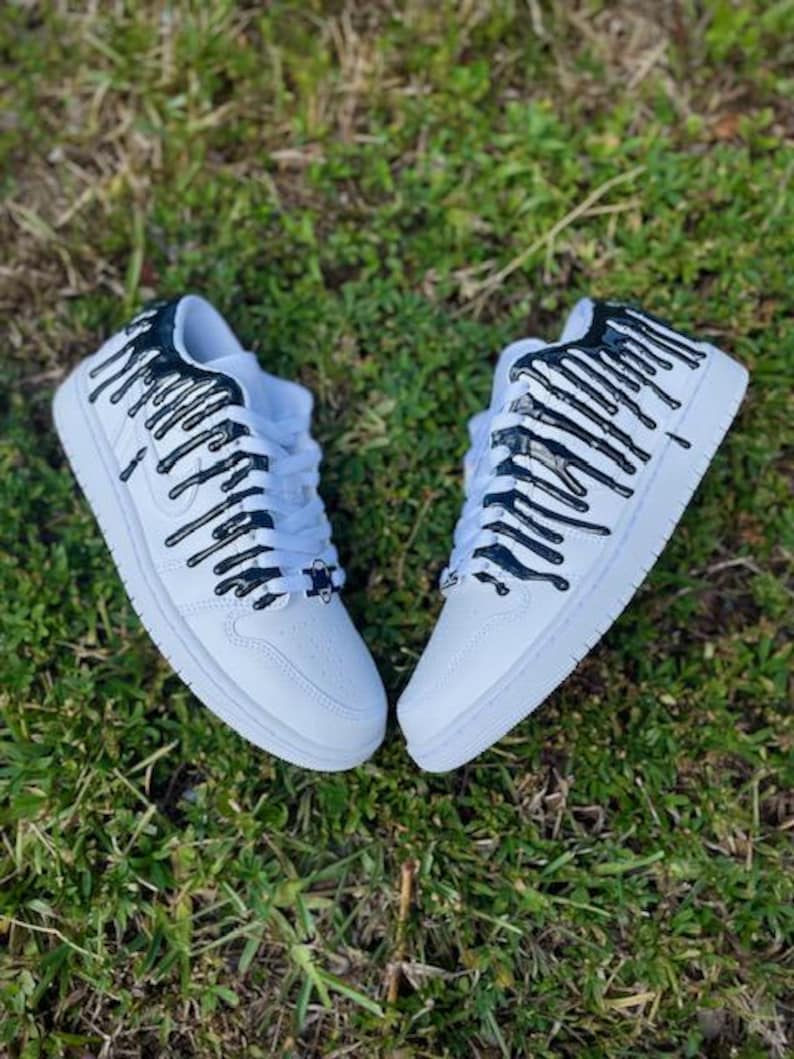 May include: White trainers with black paint dripping down the sides. The paint is in a vertical stripe pattern.