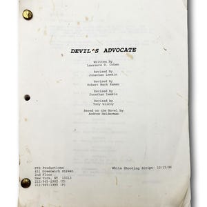 May include: A vintage, off-white film script titled "DEVIL'S ADVOCATE" with text in black font. The script is held together with brass fasteners. The text includes the writer's name, revision details, and production information. The script is dated 10/15/96.
