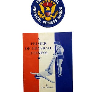 Peut inclure: Un écusson brodé circulaire avec un aigle doré et le texte Presidential Physical Fitness Award, accompagné d'un livret rectangulaire intitulé A Primer of Physical Fitness par Ann Delafield, avec une couverture aux couleurs rouge, blanc et bleu.