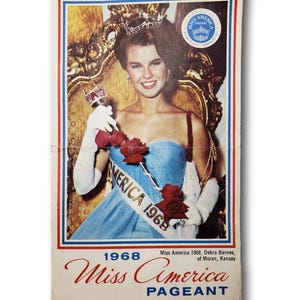 May include: A vintage Miss America Pageant program from 1968 featuring Debra Barnes. The cover shows a smiling woman in a blue dress, wearing a crown and sash that reads "America 1968". The program is bordered in red, white, and blue.