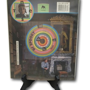 May include: A magazine cover for "NEST A QUARTERLY OF INTERIORS" is displayed on a black stand. The cover features a portrait, a colorful circular design, and the text "DJ SPOOKY PRESENTS". The magazine is labeled "FALL 2001".