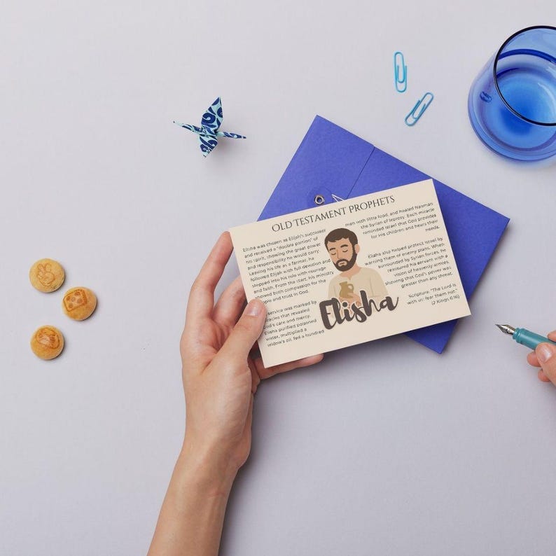 May include: A beige card with the text "Old Testament Prophets" and the name "Elisha" is held by a person. The card features an illustration of a man and text. A blue envelope, origami bird, and glass are in the background.