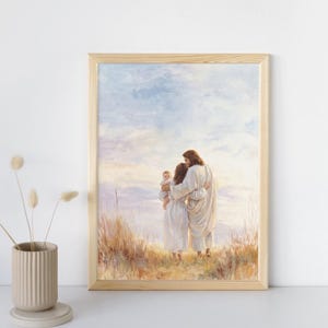 May include: A framed print depicts a tender scene of a family. A man and woman embrace, holding a baby, set against a backdrop of a serene sky and grassy field. The artwork is encased in a light-colored wooden frame.