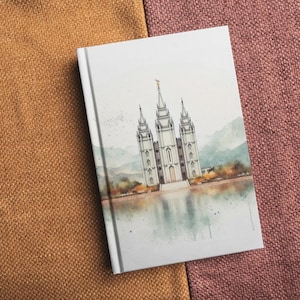 Puede incluir: Un cuaderno blanco con una ilustración de acuarela de un templo blanco con una aguja dorada, rodeado de árboles y un reflejo en el agua.