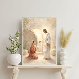 May include: Framed religious artwork depicting a biblical scene. A figure in white robes extends a hand towards a kneeling woman in a head covering and reddish-brown garment. The background shows a stone structure and soft lighting.