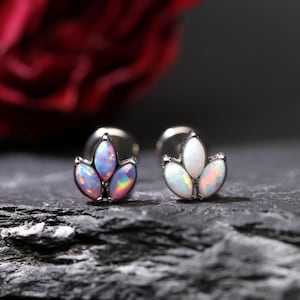 May include: A pair of stud earrings featuring a three-petal design. Each petal is an oval-shaped opal with iridescent colors of pink, blue, and green. The earrings have a silver-colored metal setting.