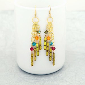 May include: Gold dangle earrings with a multi-coloured crystal and chain design. The earrings feature green, orange, blue, and red crystals.