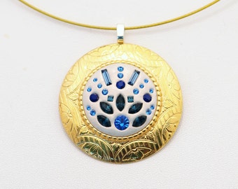 Könnte beinhalten: Eine goldene Halskette mit einem runden Anhänger, der ein weißes und blaues Blumenmuster mit blauen Strasssteinen zeigt.