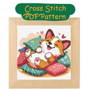 Puede incluir: Patrón de punto de cruz con un perro corgi de dibujos animados tumbado en una pila de almohadas coloridas. El corgi sonríe y tiene las patas en el aire. El patrón está en un marco de madera.
