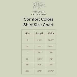 Puede incluir: Una tabla de tallas de camisas Comfort Colors de Trilium Clothing sobre fondo verde claro. La tabla enumera las tallas de S a 3XL con las medidas de largo y ancho en pulgadas. Una peque&ntilde;a ilustraci&oacute;n de una rama de olivo aparece arriba.