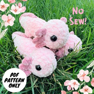 May include: Three plush pink axolotls with dark eyes and frilly gills are arranged on green grass. The axolotls are made of a soft, textured material. The words "No Sew!" and "PDF Pattern Only" are visible.