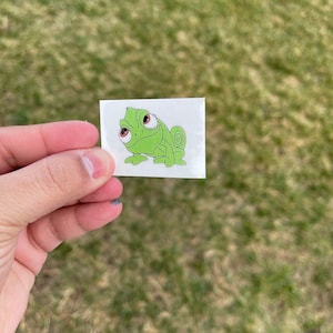 May include: A green chameleon cartoon character with large eyes and a curled tail. The character is on a white sticker.