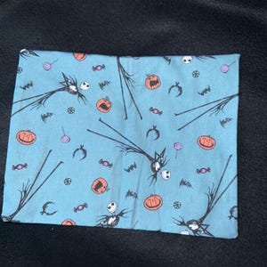 May include: A blue fabric with a repeating pattern of Jack Skellington from The Nightmare Before Christmas. The pattern also includes pumpkins, bats, candy canes, and candy.