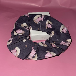 May include: A dark blue scrunchie with a repeating pattern of pink pigs on a crescent moon with yellow stars.
