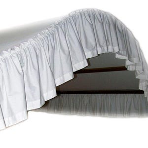 May include: White bed skirt with a ruffled edge. The skirt is draped over a bed frame and hangs down to the floor.