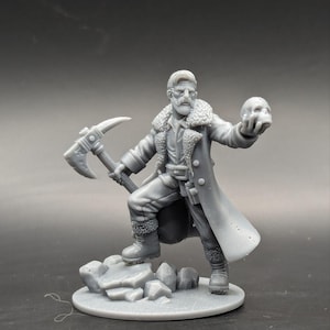 Op de afbeelding: Een grijs 3D-geprint miniatuur van een persoon die een lange jas draagt, een schedel in de ene hand en een houweel in de andere hand vasthoudt. Het miniatuur staat op een rotsachtige basis.