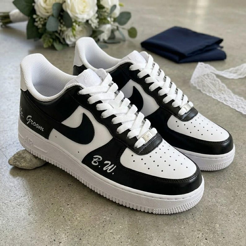 May include: Black and white sneakers with white laces. The sneakers have the words "Mr. Groom" and "B.W." written on them. The shoes have a white sole and a black swoosh.