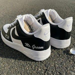May include: A pair of black and white sneakers with the Nike logo. The sneakers have white laces and soles. The words "K.W." and "Mr. Groom" are written on the sides of the shoes.