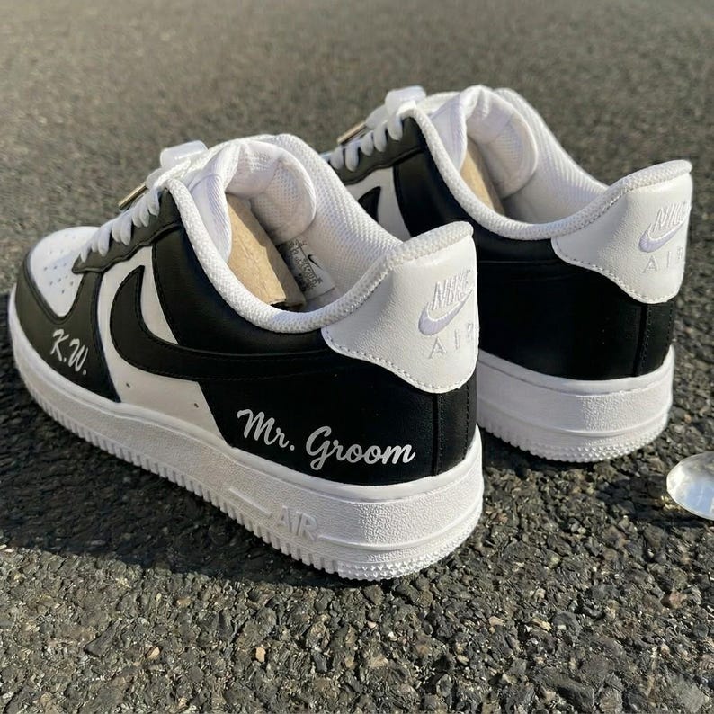 May include: A pair of black and white sneakers with the Nike logo. The sneakers have white laces and soles. The words "K.W." and "Mr. Groom" are written on the sides of the shoes.
