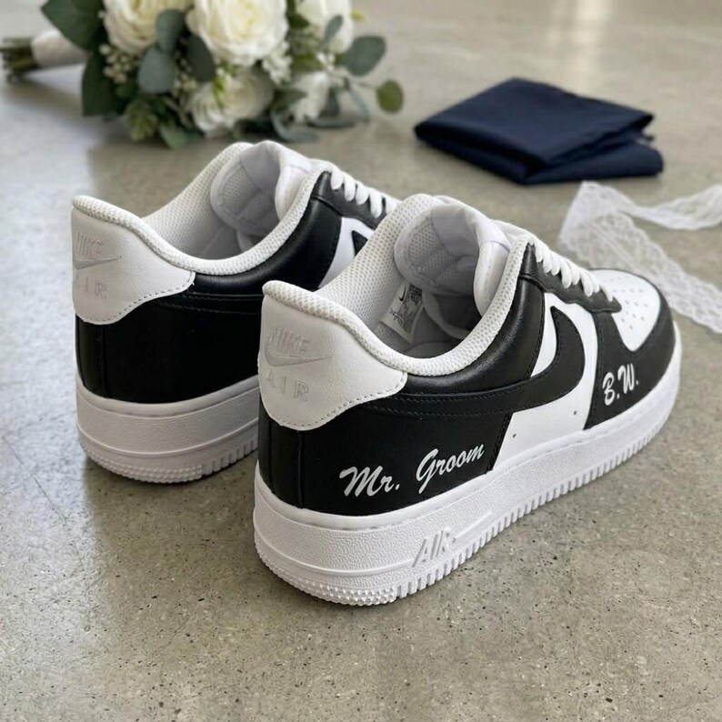 May include: Black and white sneakers with the words "Mr. Groom" and initials "B.W." written on the side. The shoes have a white sole and a black swoosh. The sneakers are part of a wedding theme.