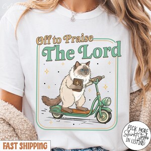 May include: White t-shirt with a graphic of a cat riding a green scooter and holding a book. The text "Off to Praise The Lord" is above the cat. Additional text reads "Pick More Shirt Styles In Listing!" and "Fast Shipping".