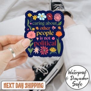 May include: A navy blue sticker with colorful floral designs and the text "caring about other people is not political." The sticker is waterproof and dishwasher safe.