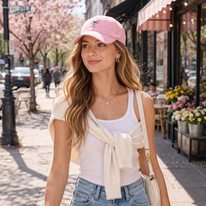 May include: A pale pink baseball cap featuring a black bow motif. The cap is made of a soft fabric and has a curved peak. The cap is worn by a person on a sunny day.