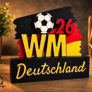 Può includere: Un espositore in legno a tema calcistico, nero, rosso e giallo. Presenta un pallone da calcio, il numero 26 e le lettere "WM" in giallo. La parola "Deutschland" è scritta in giallo sulla base.