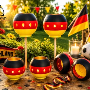 May include: A collection of decorative candle holders and ornaments in the colors of the German flag: black, red, and yellow. The candle holders are spherical with diamond-shaped cutouts. A soccer ball and German flags are also present.