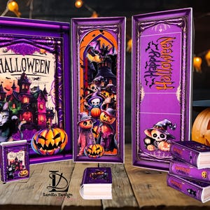 Op de afbeelding: Halloween-kunstwerk met een spookhuis, kat en pompoen. Het kunstwerk is paars omlijst en bevat het woord "Halloween". Er zijn ook verschillende kleine boeken met Halloween-ontwerpen aanwezig, samen met een uitgesneden pompoen.