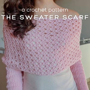 Könnte beinhalten: Ein hellrosa gehäkelter Sweater-Schal mit langen Ärmeln. Der Text "a crochet pattern THE SWEATER SCARF" ist auf dem Bild zu sehen. Der Sweater-Schal wird über einem weißen Oberteil getragen.