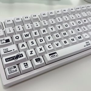 May include: A white mechanical keyboard with black keycaps featuring various symbols and text, including "404", "Tab", "Caps Lock", "Shift", "Ctrl", "Digital", and "Win".