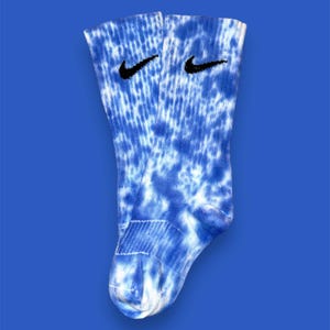 Peut inclure: Une paire de chaussettes en tie-dye bleu et blanc avec un logo Nike noir en forme de virgule sur chaque chaussette.
