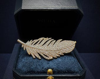 May include: A gold feather brooch with clear rhinestones, displayed in a black velvet box with a gold trim.