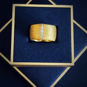 Peut inclure: Une bague en or avec une finition brossée et une rangée de diamants clairs sertis au centre.