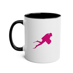 May include: White ceramic mug with a black handle and interior. A magenta silhouette of a scuba diver is printed on the side. The mug is designed for hot or cold beverages.