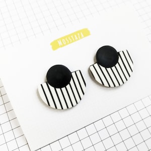 May include: A pair of black and white striped earrings with a black circle in the centre of each earring. The earrings are on a white card with the word "MOSSTAZA" written in yellow.