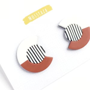 May include: A pair of geometric earrings with a white, black, and terracotta color scheme. The earrings are shaped like a half-circle with a black and white striped circle in the center.