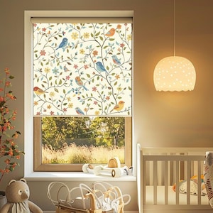 May include: A white crib with a white and brown patterned blanket in a nursery with a window featuring a white roller shade with a floral and bird design.