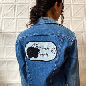 Può includere: Giacca di jeans blu chiaro con una toppa a forma di pecora nera sul retro. La toppa presenta il testo "Baa... Baa..." e "Have You Any??". La giacca ha un colletto classico, chiusura con bottoni e una gonna a quadri colorata.